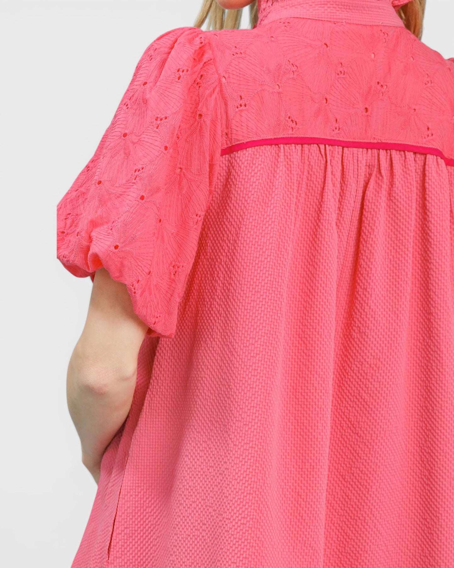 Close-up of a pink blouse with intricate detailing on a white background