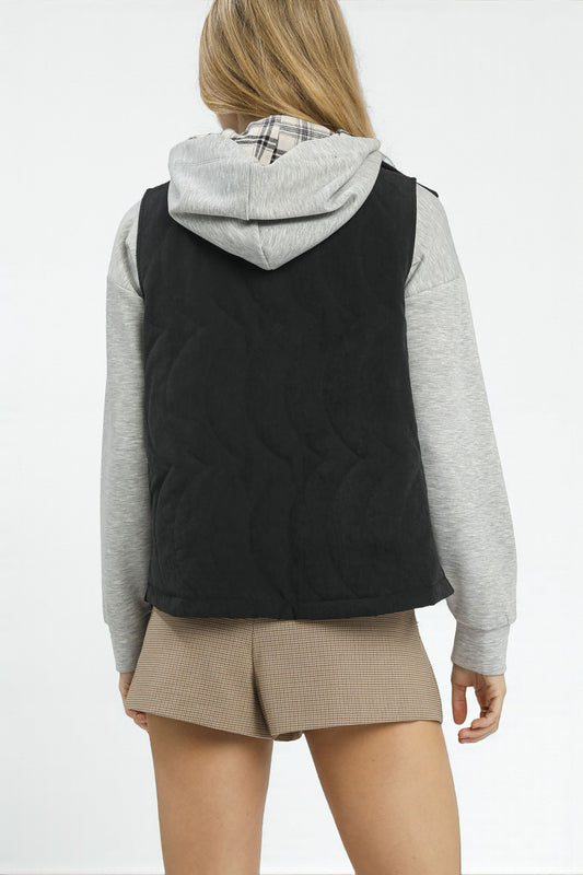 Person wearing a black quilted vest over a gray hoodie on a white background