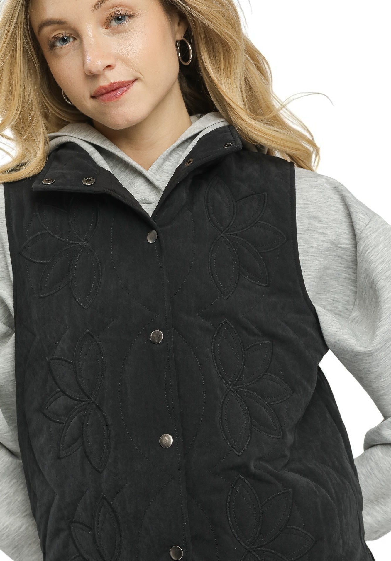 Person wearing a black quilted vest over a gray sweater on a white background