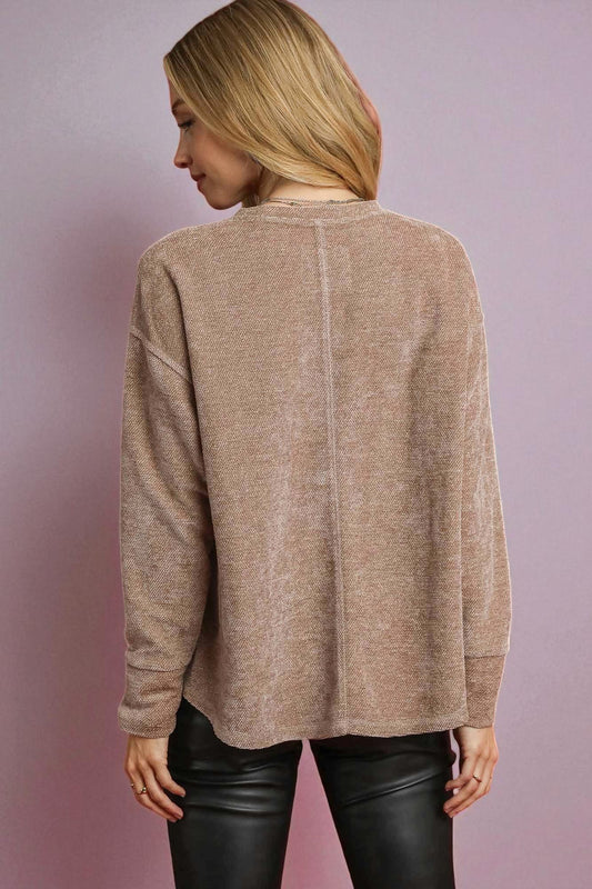 Person wearing a beige sweater and black pants against a pink background