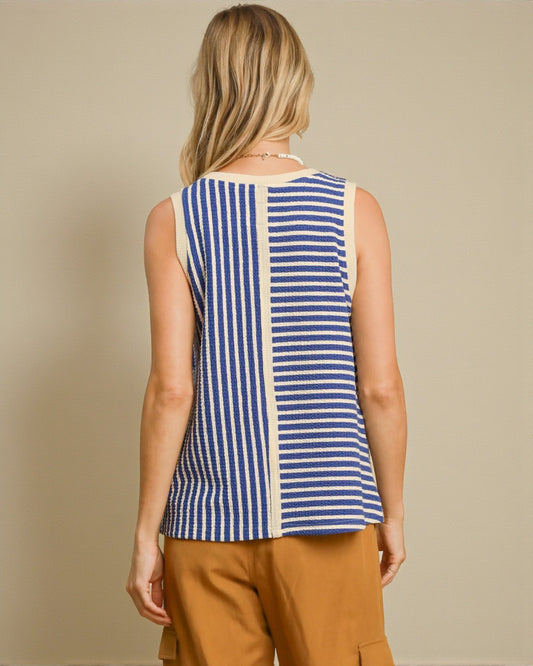 Woman wearing a blue and white striped sleeveless top with brown pants on a beige background