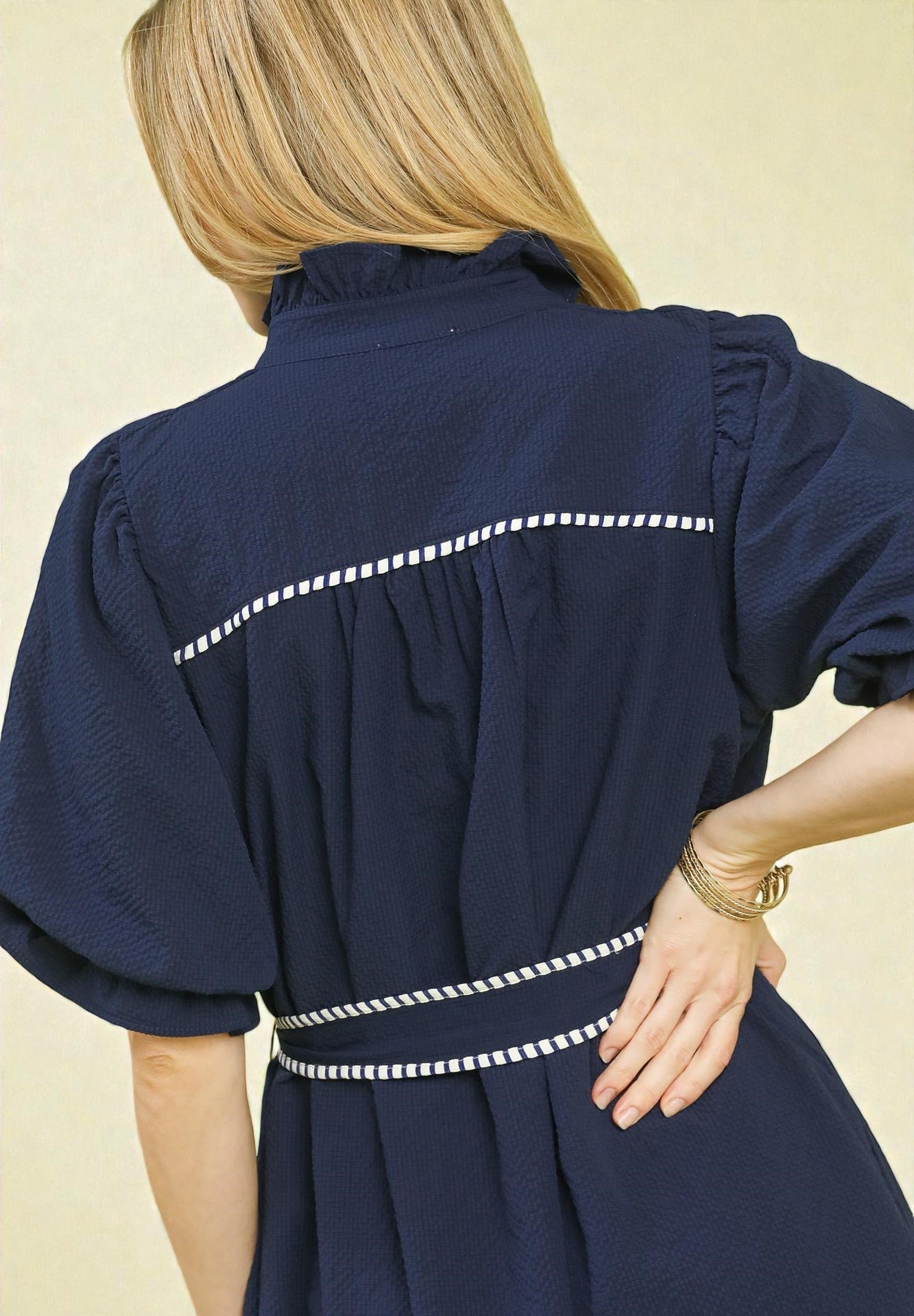 Navy dress with white trim worn by a person on a beige background