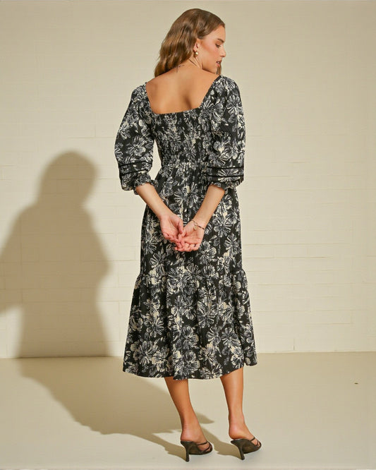 Woman wearing a black floral dress against a plain background