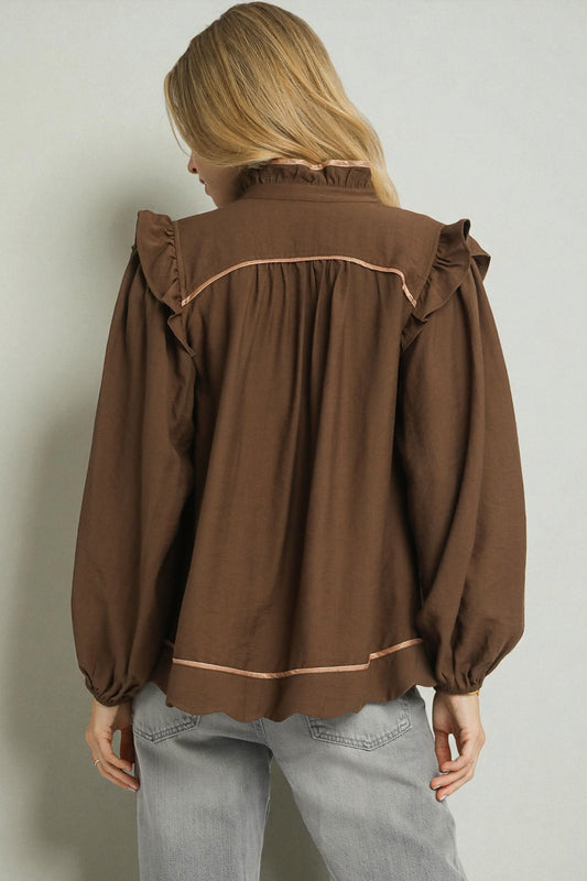 Brown blouse with ruffled details worn by a person against a plain background