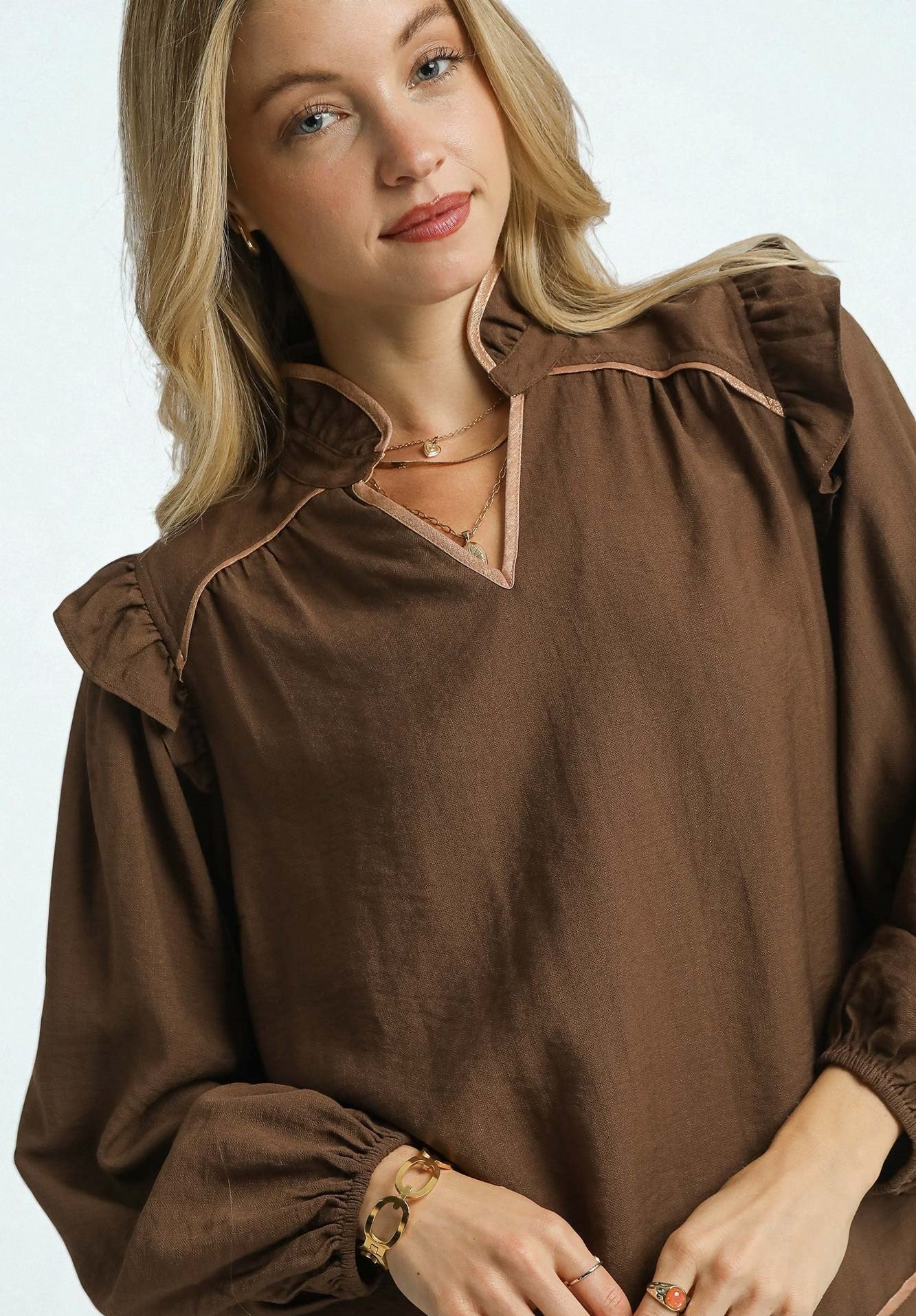 Woman wearing a brown blouse with ruffled collar on a white background