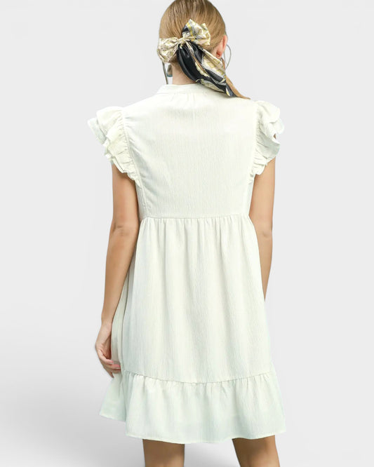 Woman wearing a white dress with ruffled sleeves on a plain background