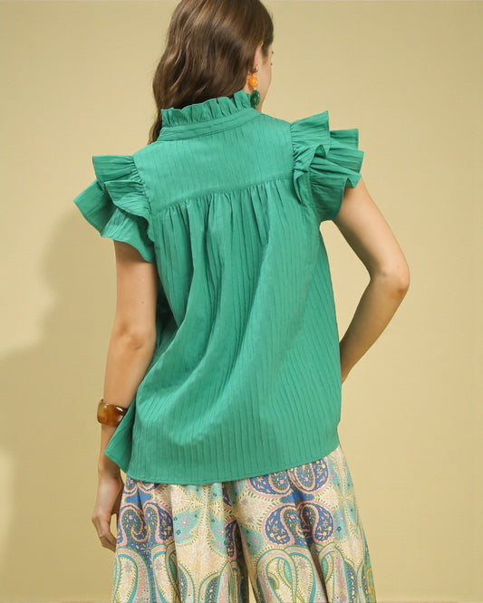 Woman wearing a green blouse with ruffled sleeves against a beige background