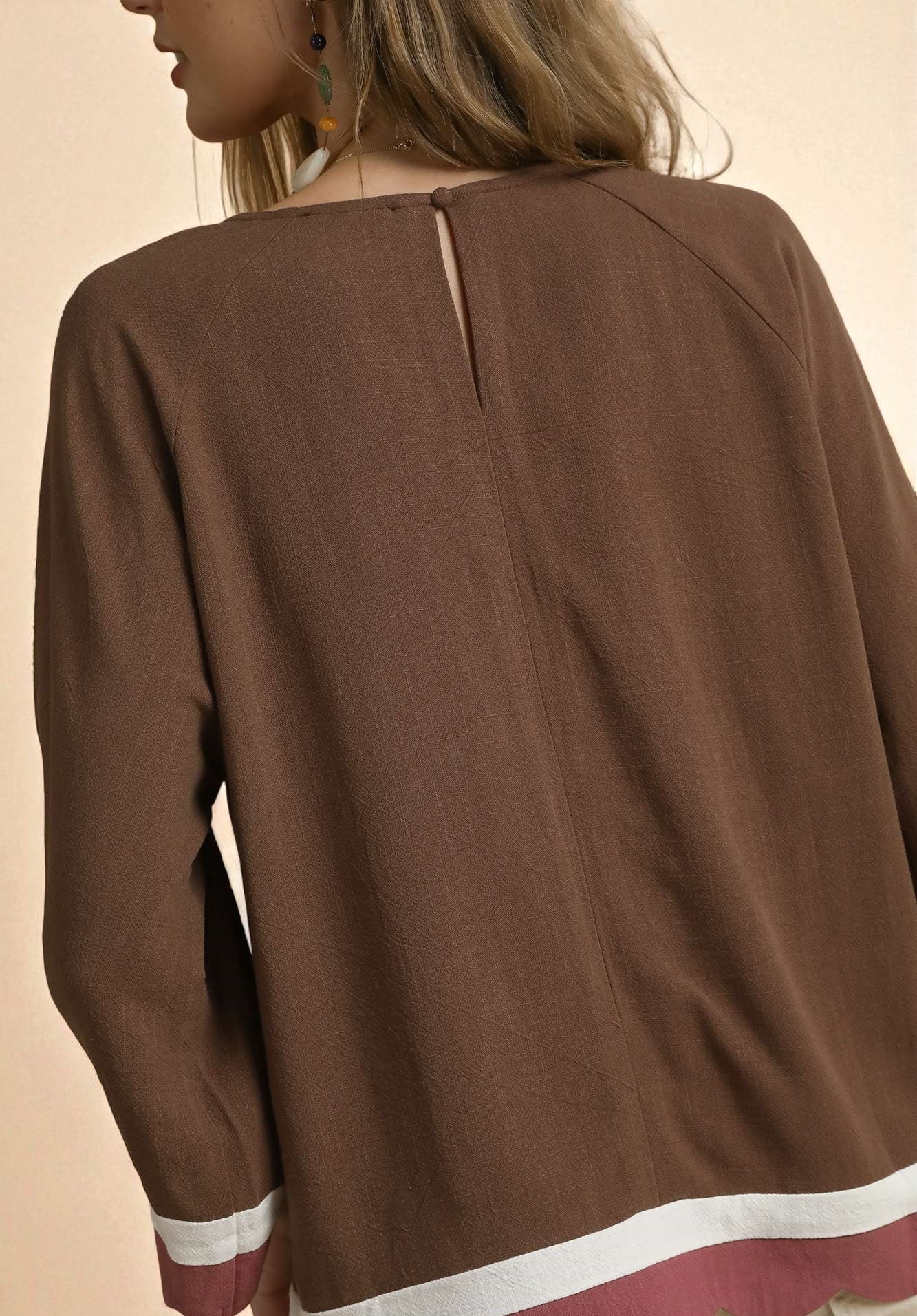 Brown blouse with white trim on a beige background