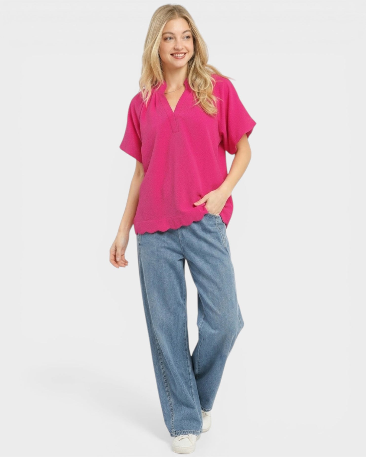 Woman wearing a bright pink top and blue jeans on a white background