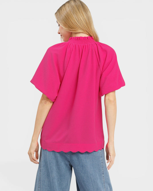 Woman wearing a bright pink blouse with scalloped hem on a white background
