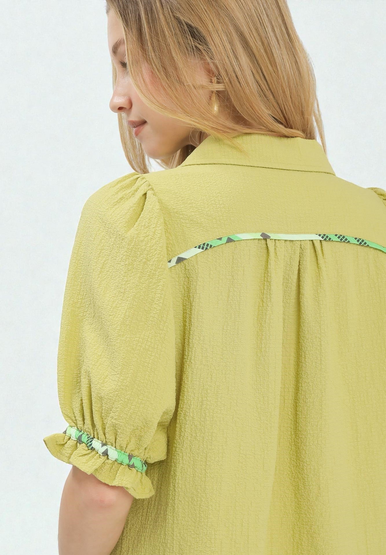 Woman wearing a mustard yellow blouse with green trim on a white background