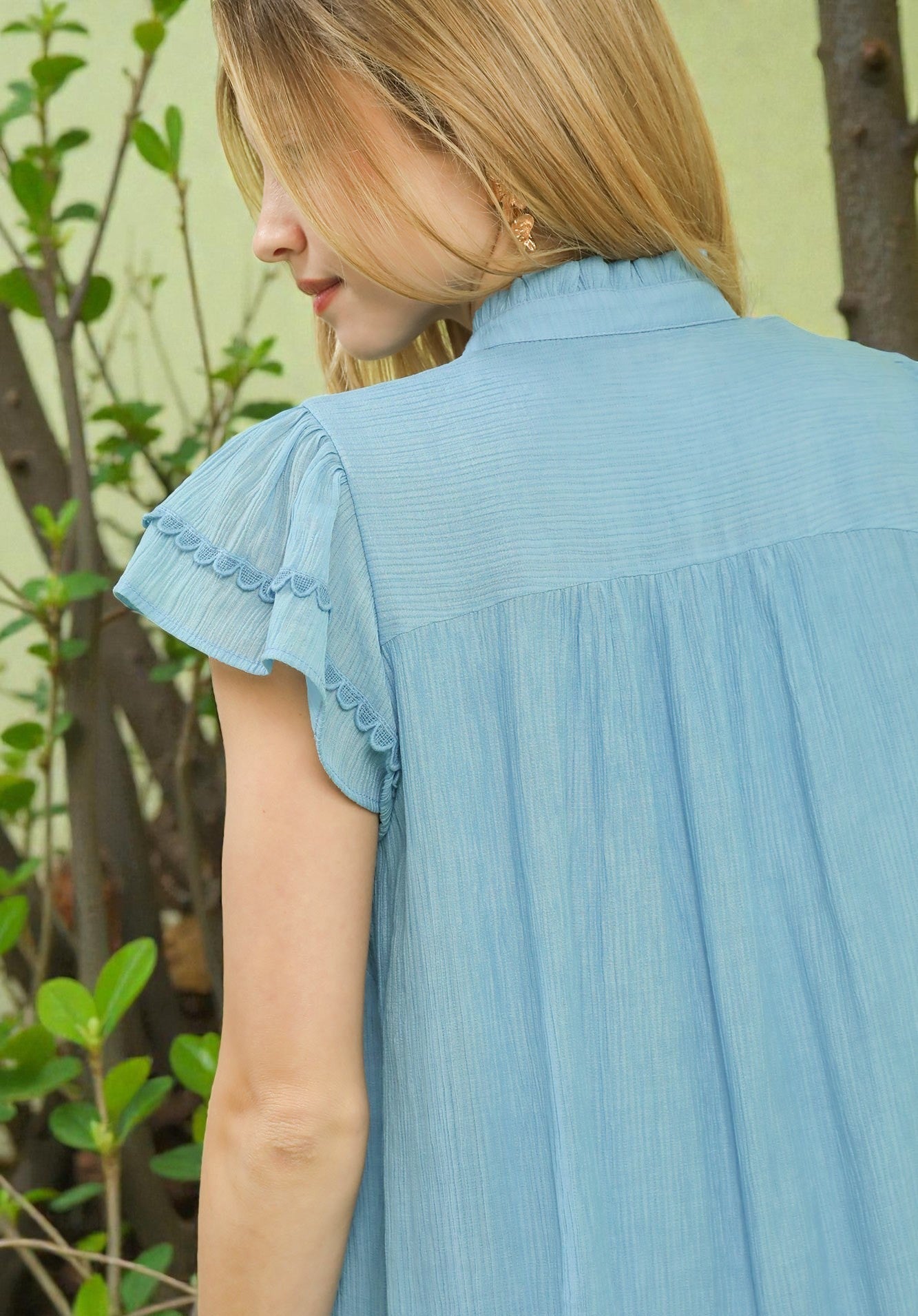 Woman wearing a light blue dress with ruffled sleeves against a blurred green background