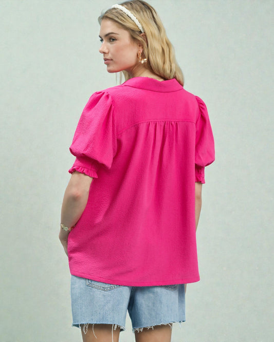 Woman wearing a bright pink blouse with ruffled sleeves on a plain background