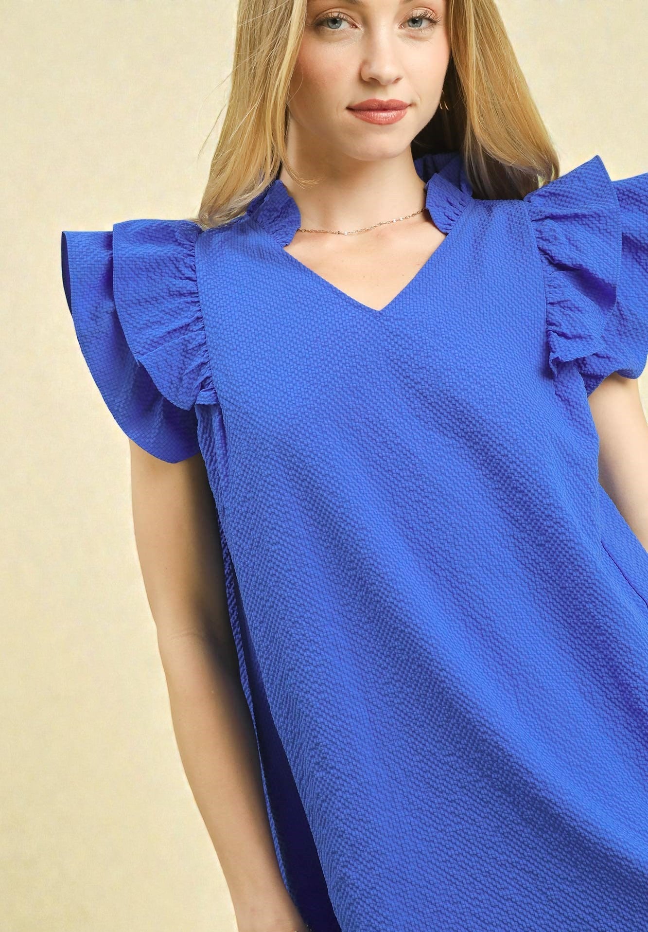 Woman wearing a blue dress with ruffled sleeves against a beige background