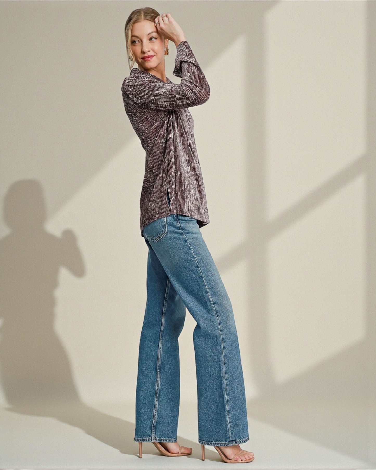 Woman wearing a patterned shirt and blue jeans against a neutral background