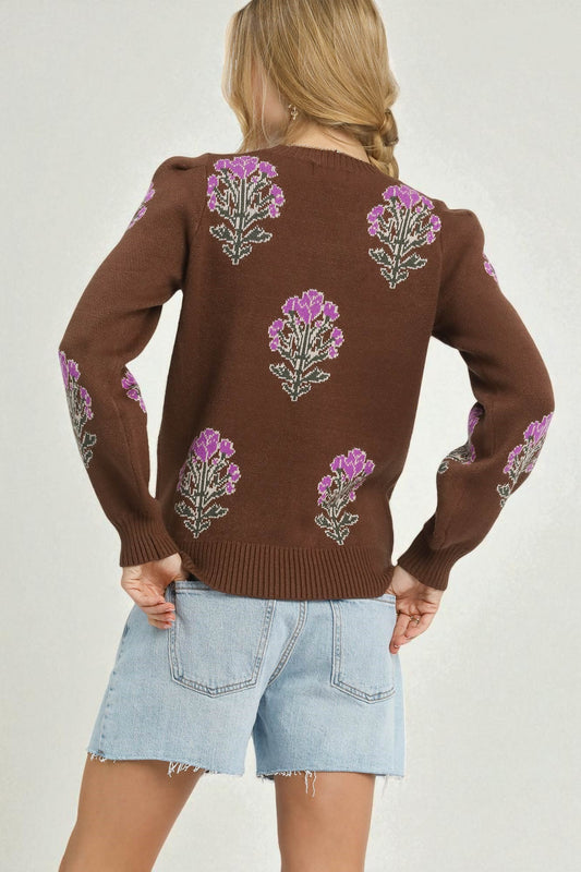 Brown sweater with floral patterns worn by a person on a plain background