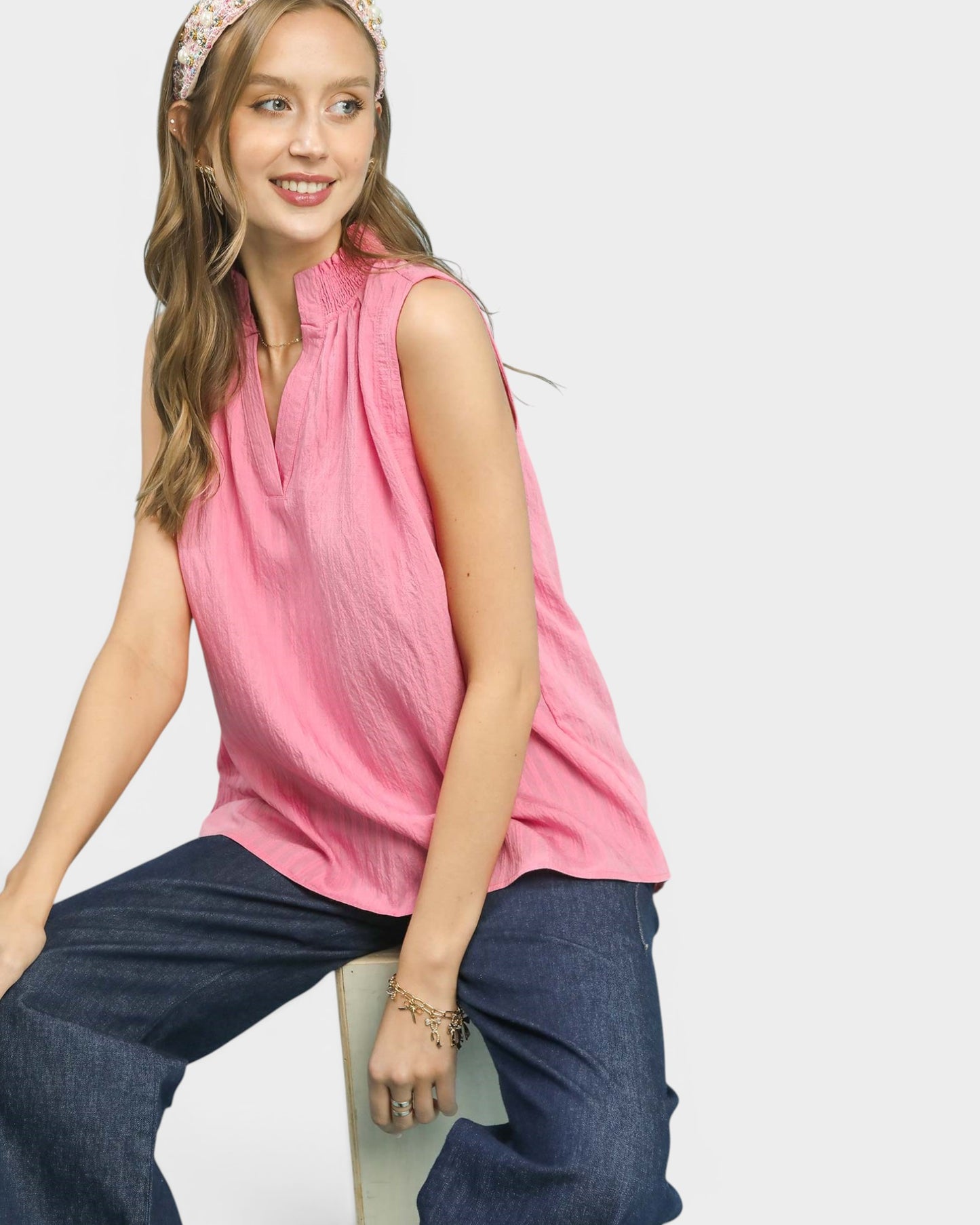 Woman wearing a pink sleeveless top and blue pants on a white background