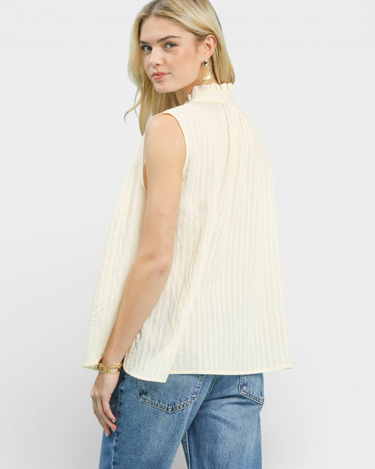 Woman wearing a sleeveless cream ribbed top and blue jeans on a white background