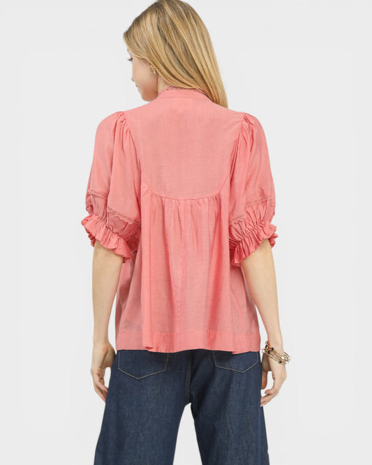 Woman wearing a coral blouse with ruffled sleeves on a white background