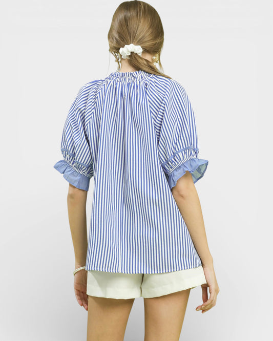 Woman wearing a blue and white striped shirt with rolled-up sleeves on a plain background