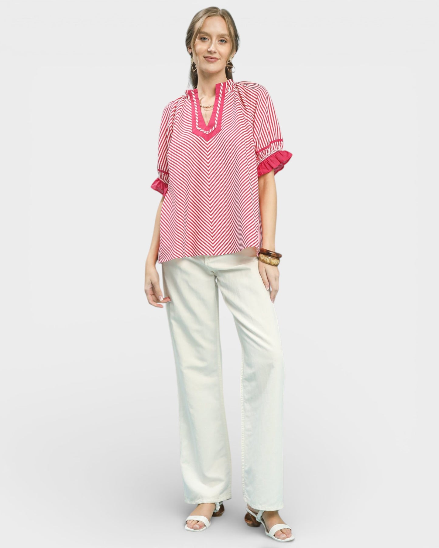 Woman wearing a red and white patterned top with white pants on a light gray background