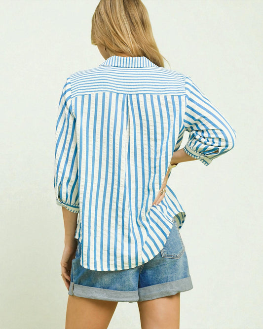 Person wearing a blue and white striped shirt with rolled-up sleeves and denim shorts on a plain background