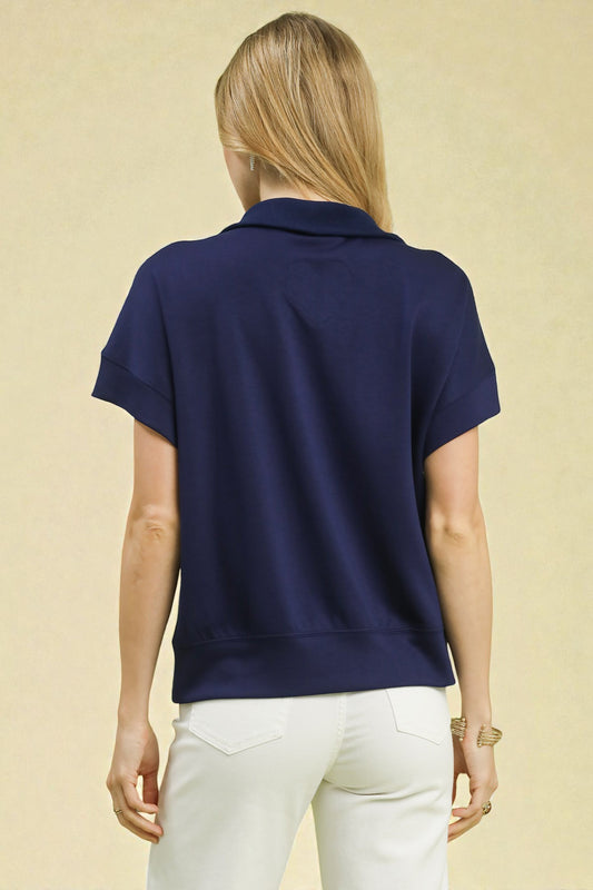 Person wearing a navy blue polo shirt and white pants on a beige background