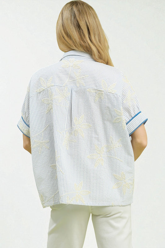 Person wearing a light blue and white striped shirt with floral patterns on a plain background