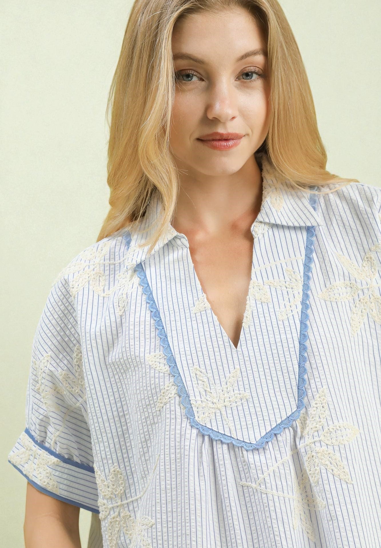 Woman wearing a light blue and white striped shirt with embroidered details on a plain background