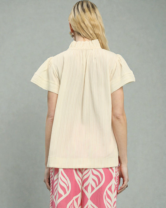 Woman wearing a beige short-sleeve blouse and pink pants with white patterns on a gray background