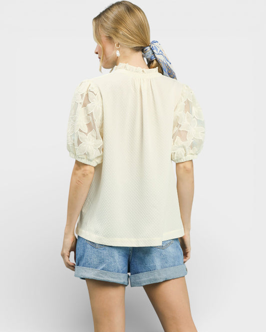 Woman wearing a light-colored blouse with sheer sleeves and denim shorts on a white background