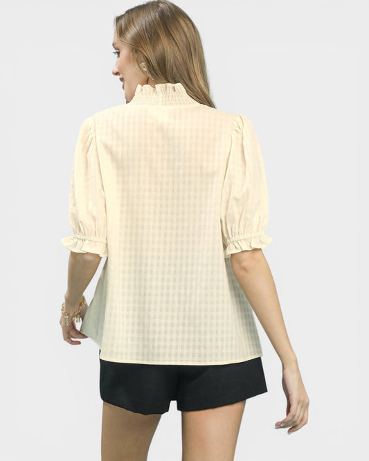 Woman wearing a light yellow textured blouse and black shorts on a white background