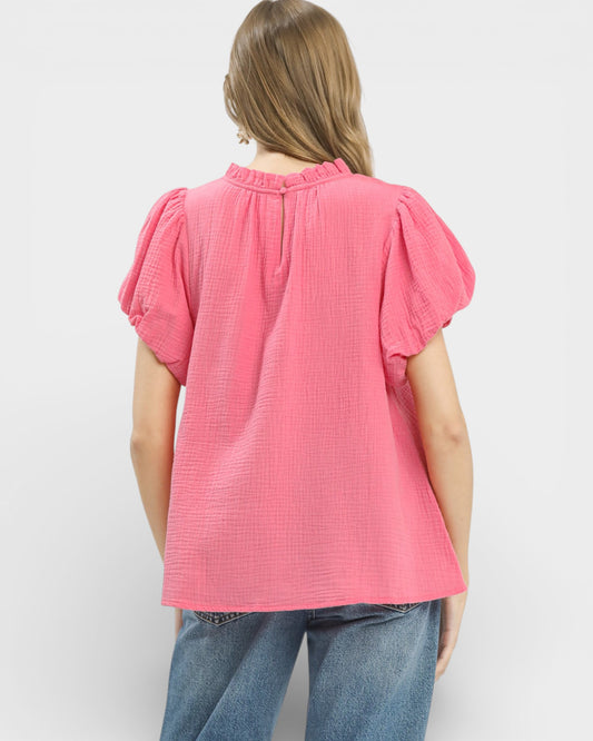 Person wearing a pink textured blouse with short sleeves on a white background