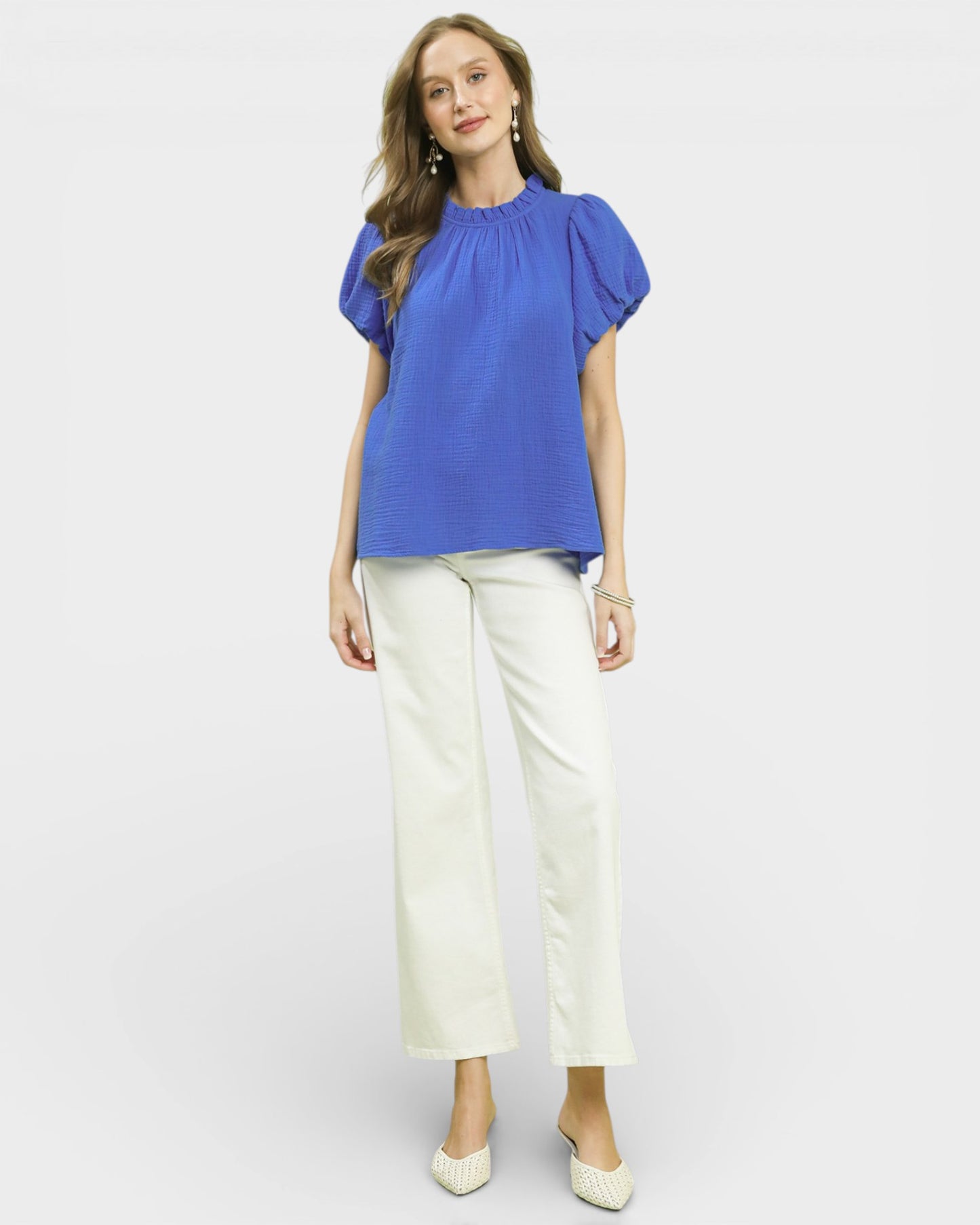 Woman wearing a blue blouse and white pants on a white background
