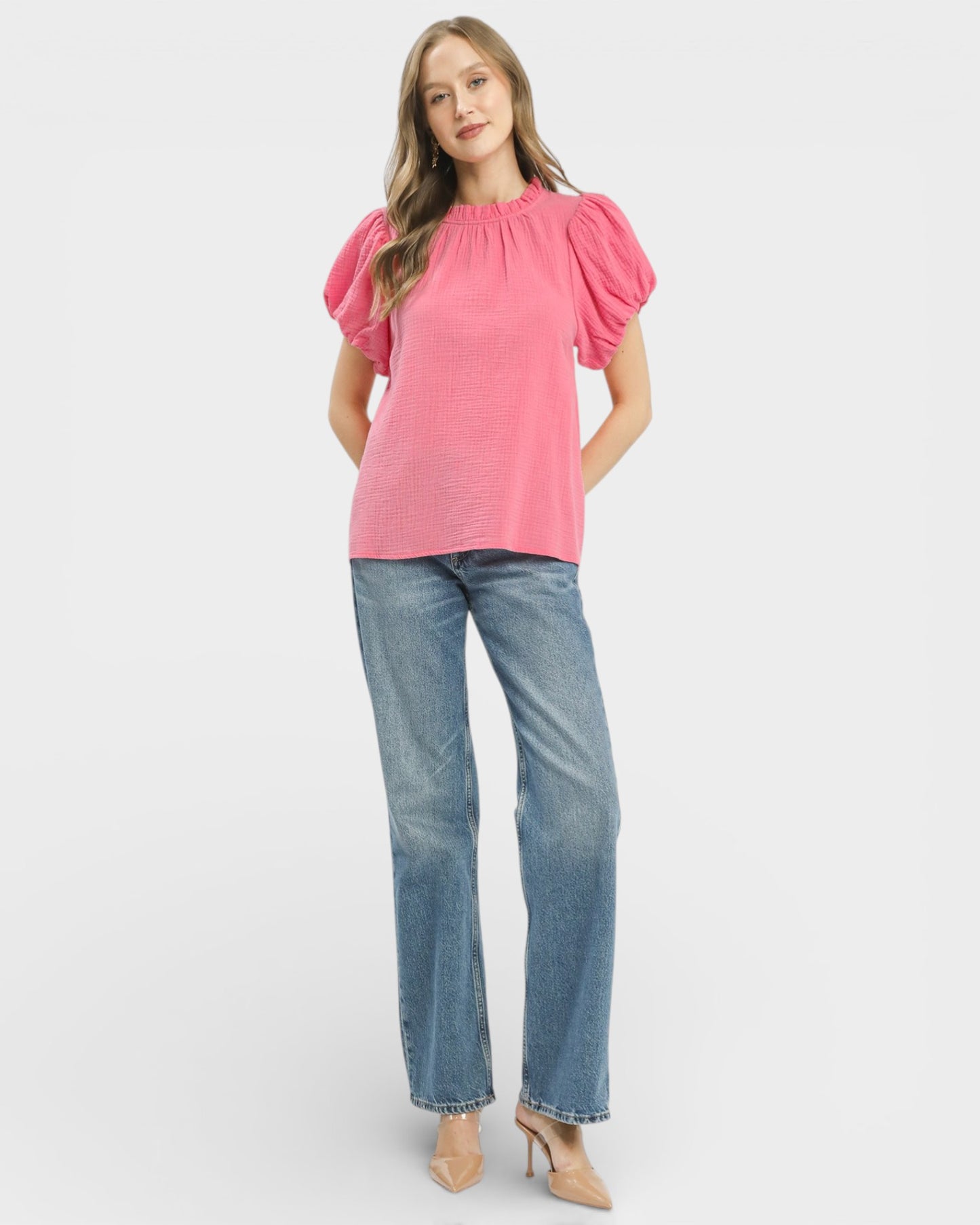 Woman wearing a pink blouse with puff sleeves and blue jeans on a white background