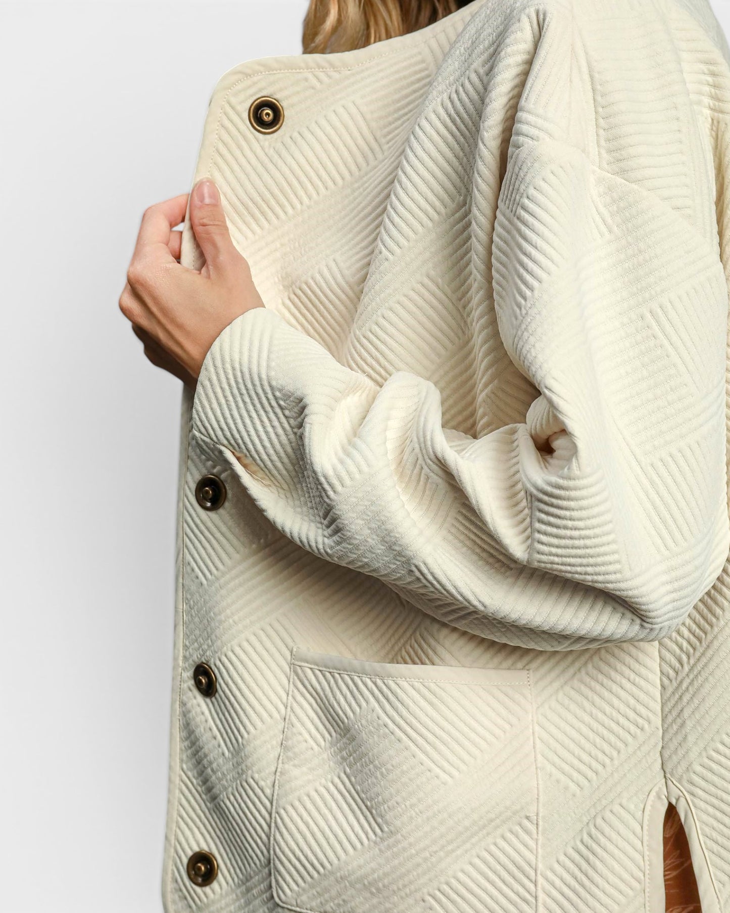 Close-up of a person wearing a textured cream-colored coat with buttons on a white background