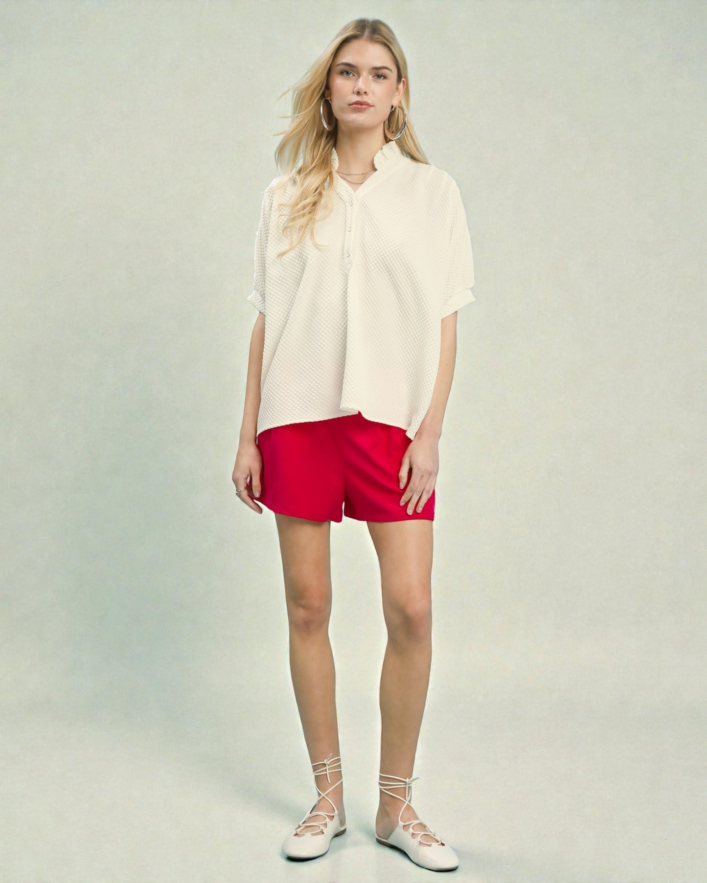 Woman wearing a white blouse and red shorts on a plain background