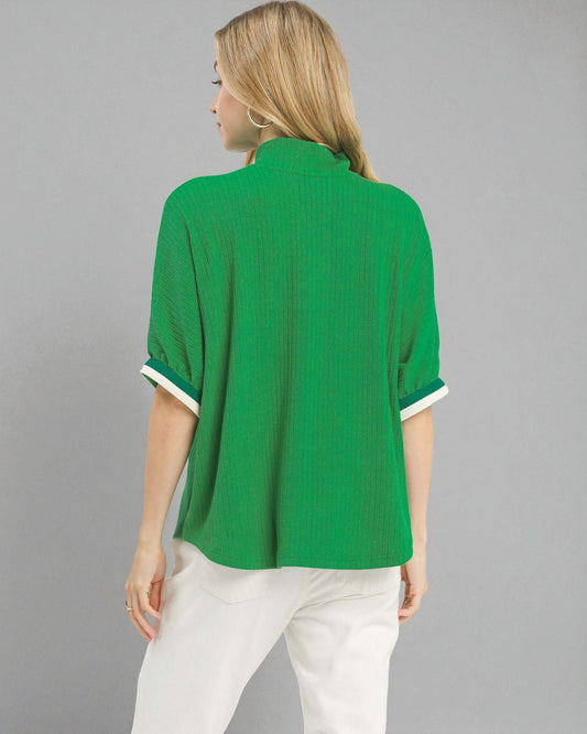 Woman wearing a green blouse with white trim on a gray background