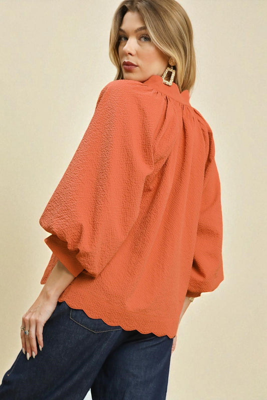 Woman wearing an orange blouse with scalloped edges on a beige background