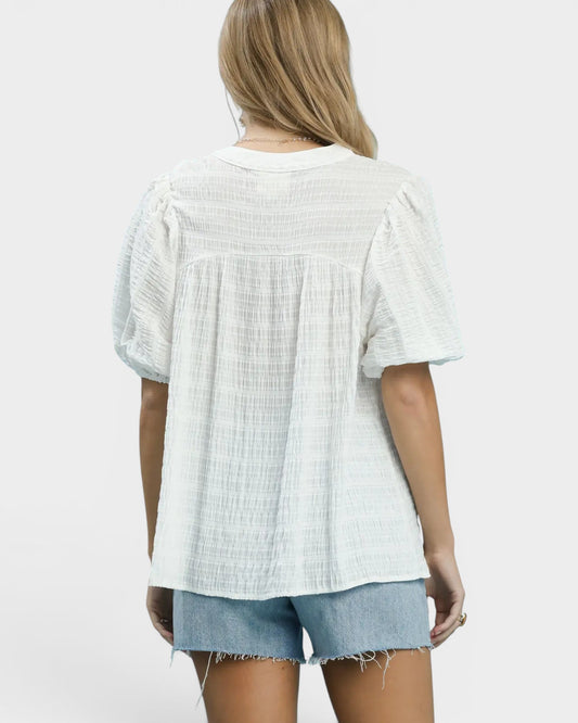 Person wearing a light-colored textured blouse and denim shorts on a white background