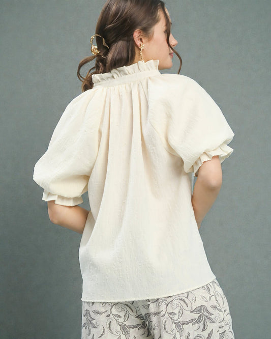 Woman wearing a cream blouse with ruffled sleeves against a gray background