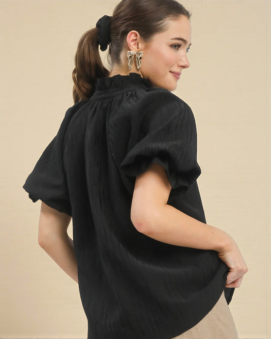 Woman wearing a black blouse with puffed sleeves against a beige background