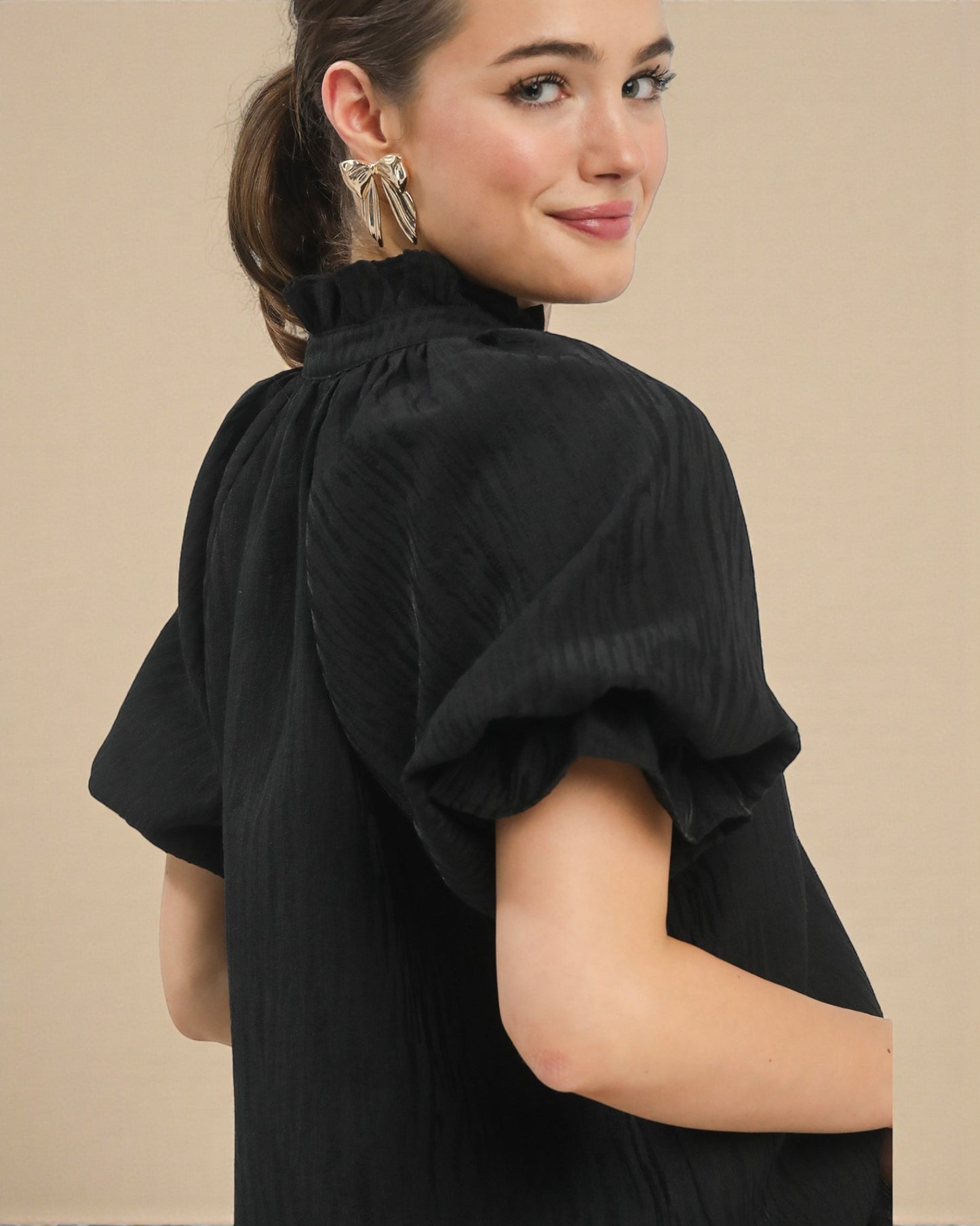 Woman wearing a black dress with puffed sleeves against a beige background