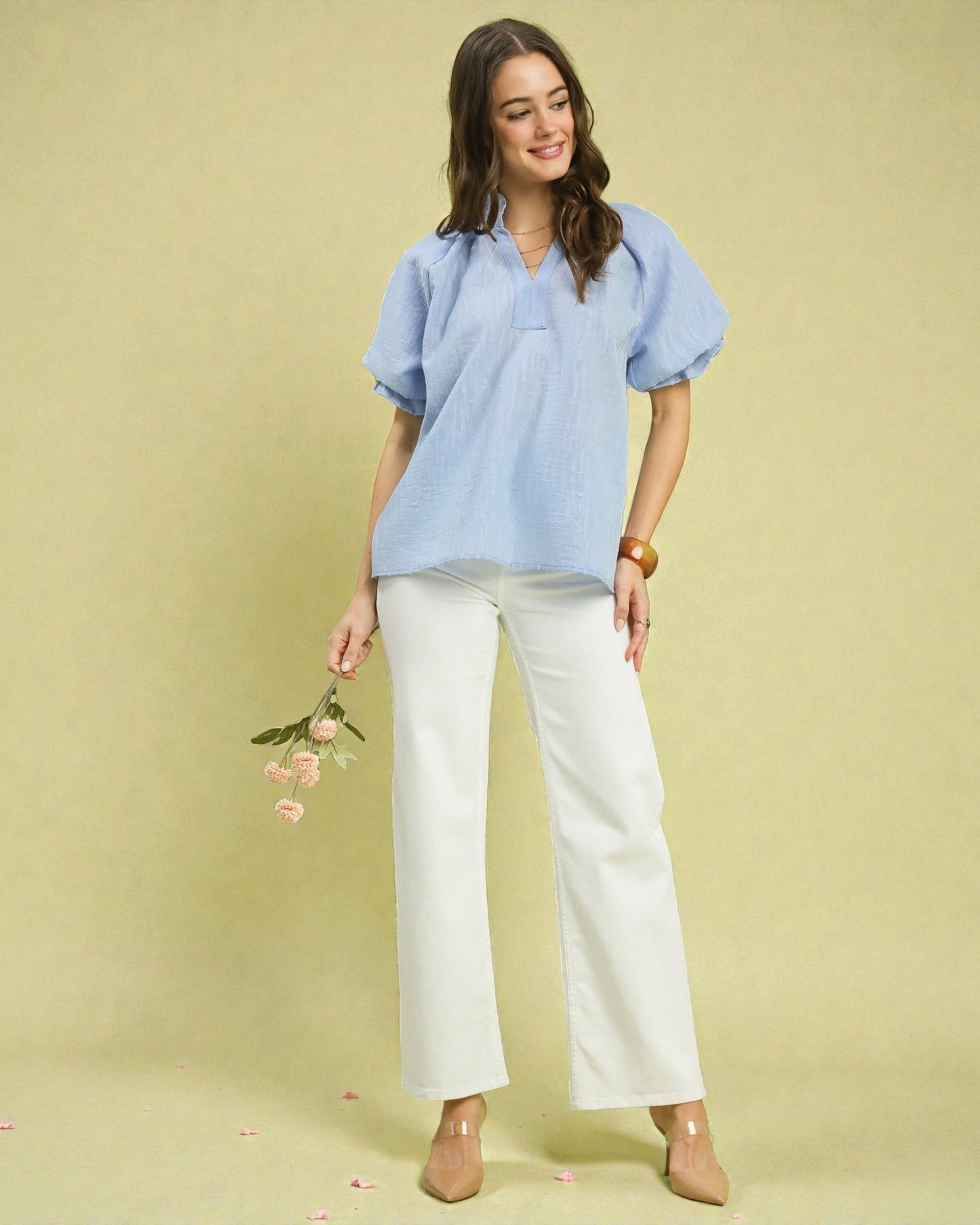 Woman wearing a light blue blouse and white pants against a beige background