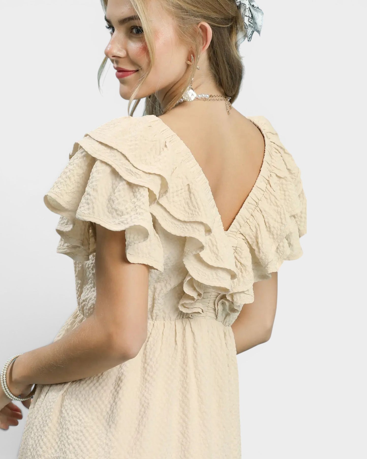Woman wearing a beige lace dress with ruffled sleeves on a white background