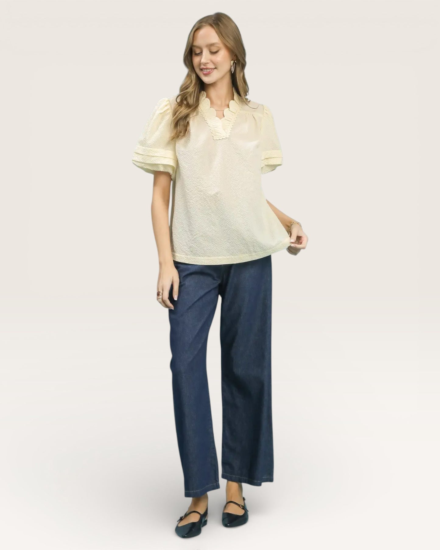 Woman wearing a light-colored blouse and dark blue pants on a white background