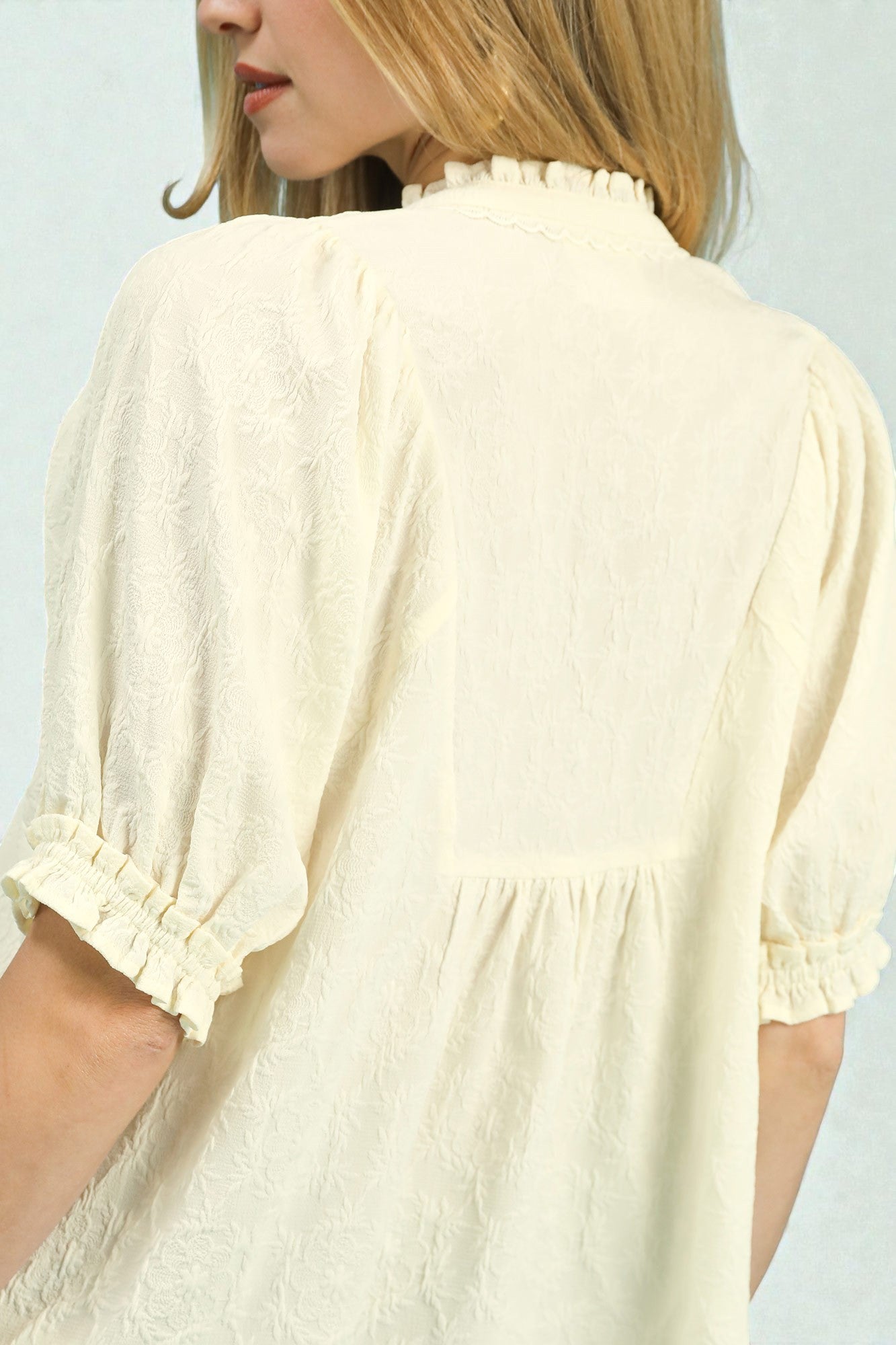 Close-up of a person wearing a cream-colored blouse with ruffled details on a light gray background