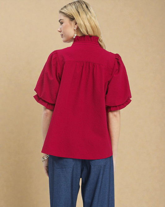 Woman wearing a red blouse with ruffled sleeves against a beige background