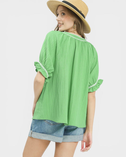 Woman wearing a green blouse with ruffled sleeves and denim shorts on a white background