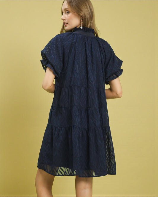 Woman wearing a navy blue dress with lace details on a yellow background